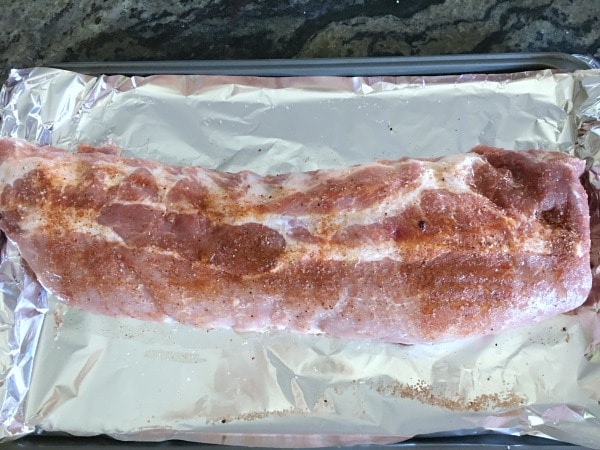 Spice rub on a raw rack of ribs. The ribs are on a baking sheet.