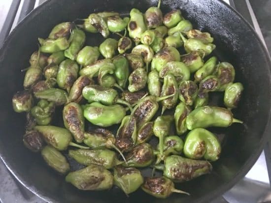 Cooking padron peppers in a cast iron pan over high heat.