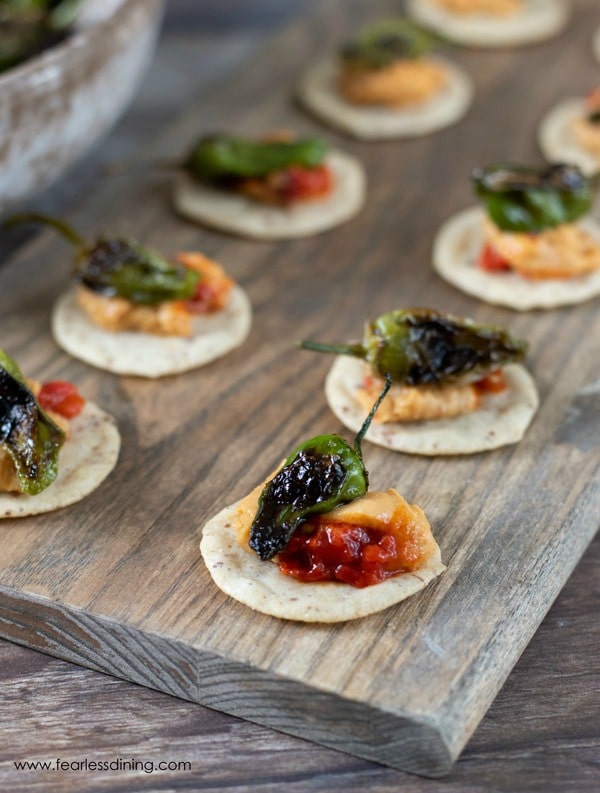 another view of a padron pepper appetizer on crackers. They are sitting on a long wooden serving platter