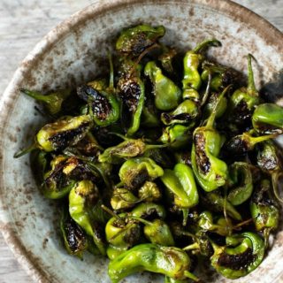 a serving bowl filled with roasted padron peppers.