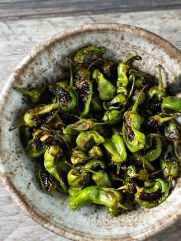 a serving bowl filled with roasted padron peppers.