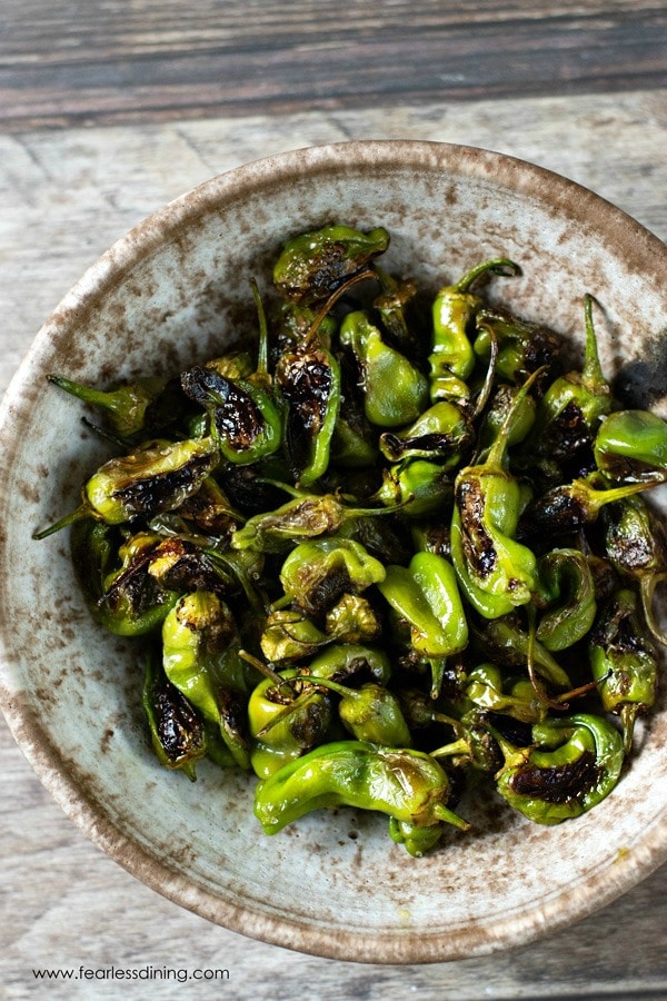 A serving bowl filled with roasted padron peppers.