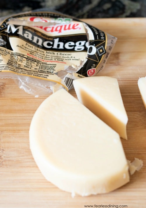 Cutting the manchego cheese into pieces on a wooden cutting board.