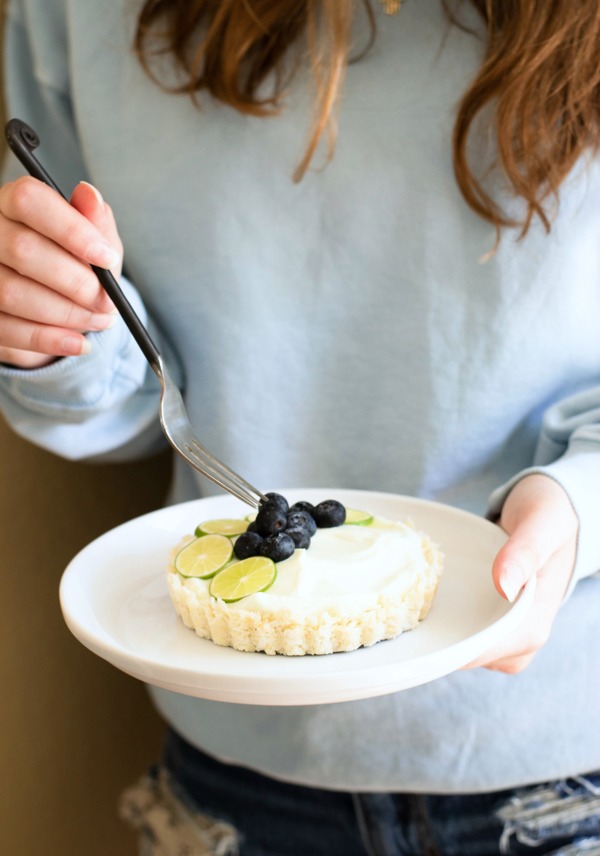 Holding a plate with a Key Lime Tart. A fork is being pressed down onto a blueberry.