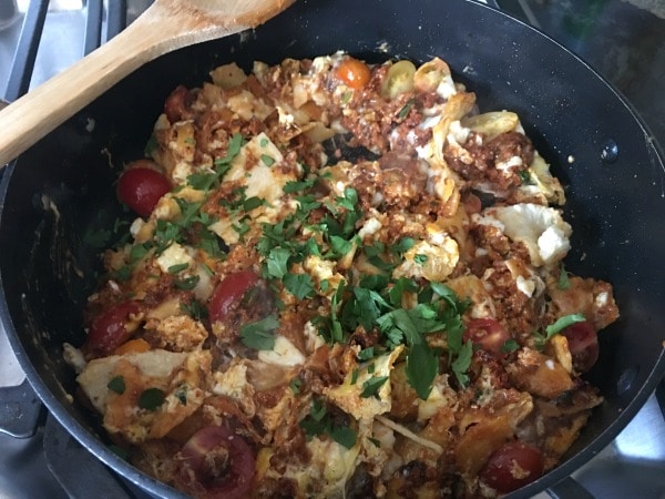 Adding cilantro to the cooked migas in the frying pan.