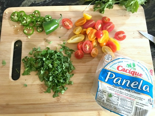Chopped cilantro, tomatoes and jalapeños on a wooden cutting board.