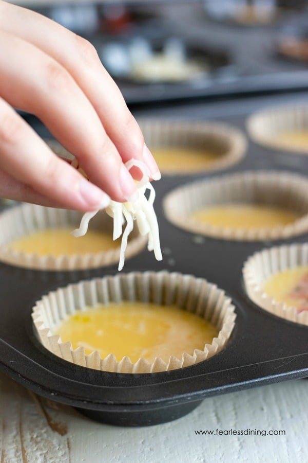 A hand dropping shredded cheese into an egg muffin cup.