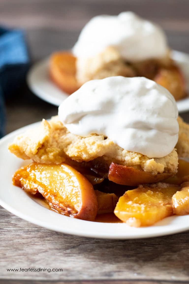 Two servings of gluten free peach cobbler on small white plates.