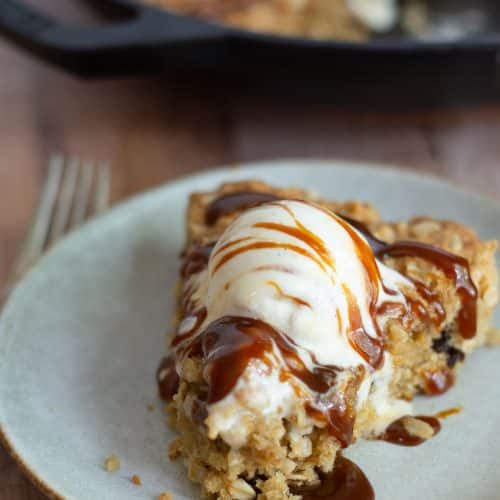 A slice of gluten-free oatmeal pizookie on a plate with ice cream and caramel sauce.