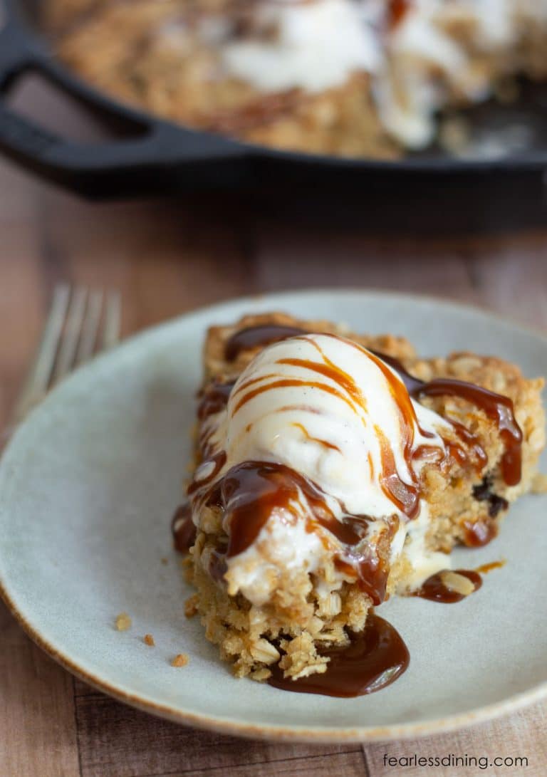 A slice of gluten-free oatmeal pizookie on a plate with ice cream and caramel sauce.
