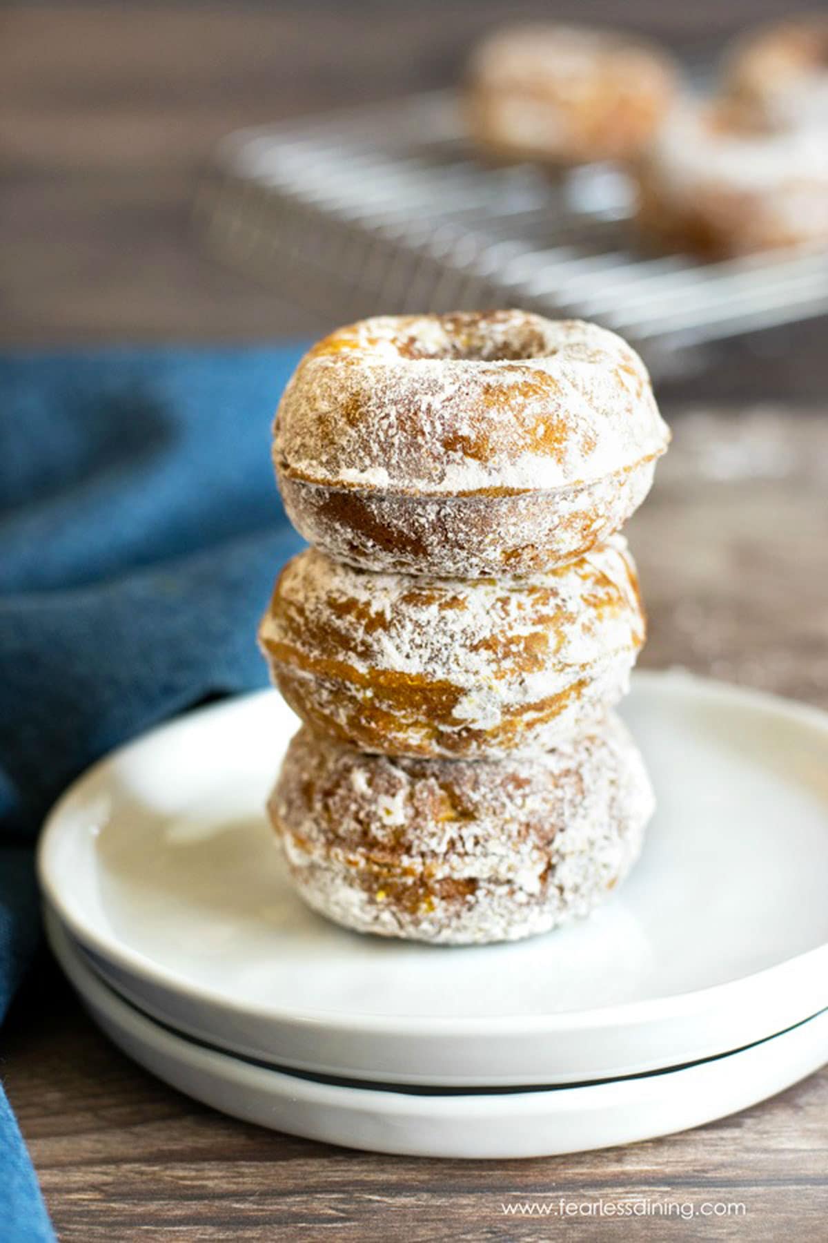 A stack of three mini gluten free pumpkin donuts on a white plate.