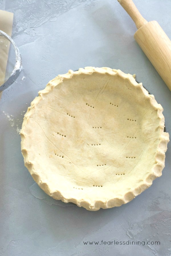 A baked pie crust on the table next to a wooden rolling pin.