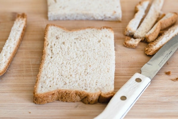 A slice of bread on a cutting board. The crust has been cut off the bread.