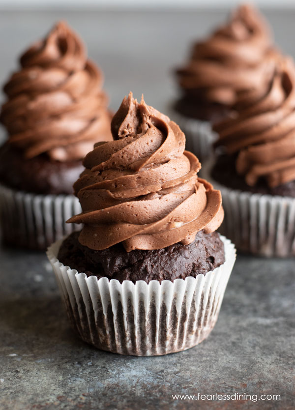 Four frosted gluten free chocolate cupcakes on a counter.