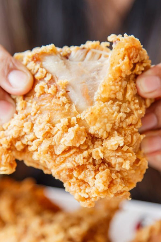 Two hands pulling apart a piece of gluten free fried chicken.