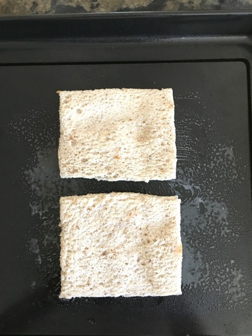 Two slices of bread on a baking pan with the crusts removed.