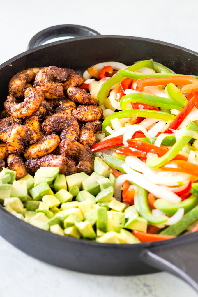 Shrimp, peppers and onions and avocado in a pan.