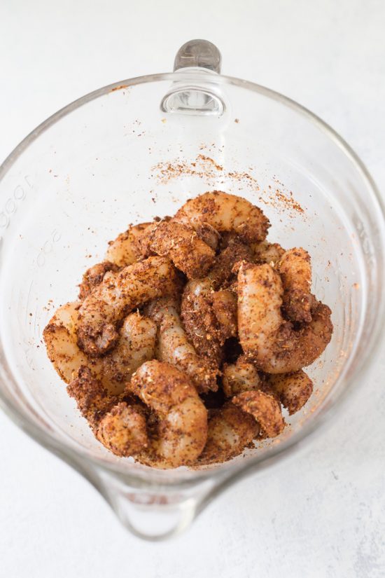 Raw shrimp and blackened seasoning in a glass bowl.