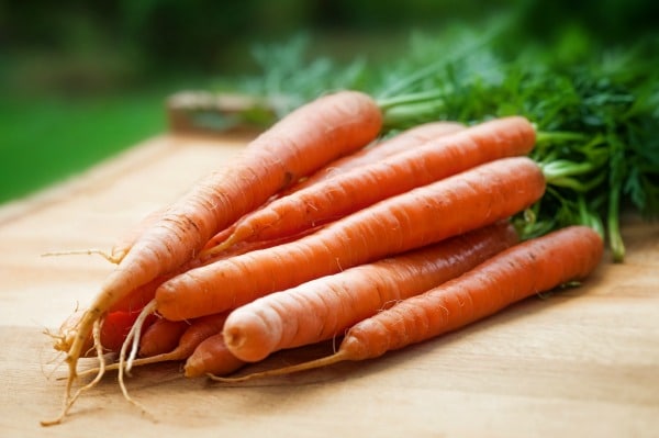 A bunch of carrots on a cutting board about to be cut.