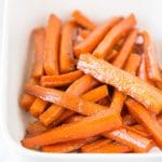 A white casserole baking dish full of cooked brown sugar carrots.