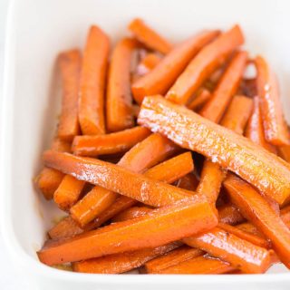 A white casserole baking dish full of cooked brown sugar carrots.