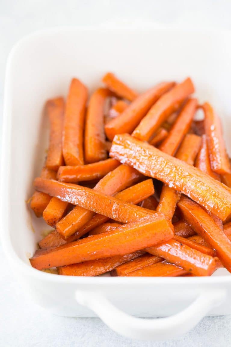 A white casserole baking dish full of cooked brown sugar carrots.
