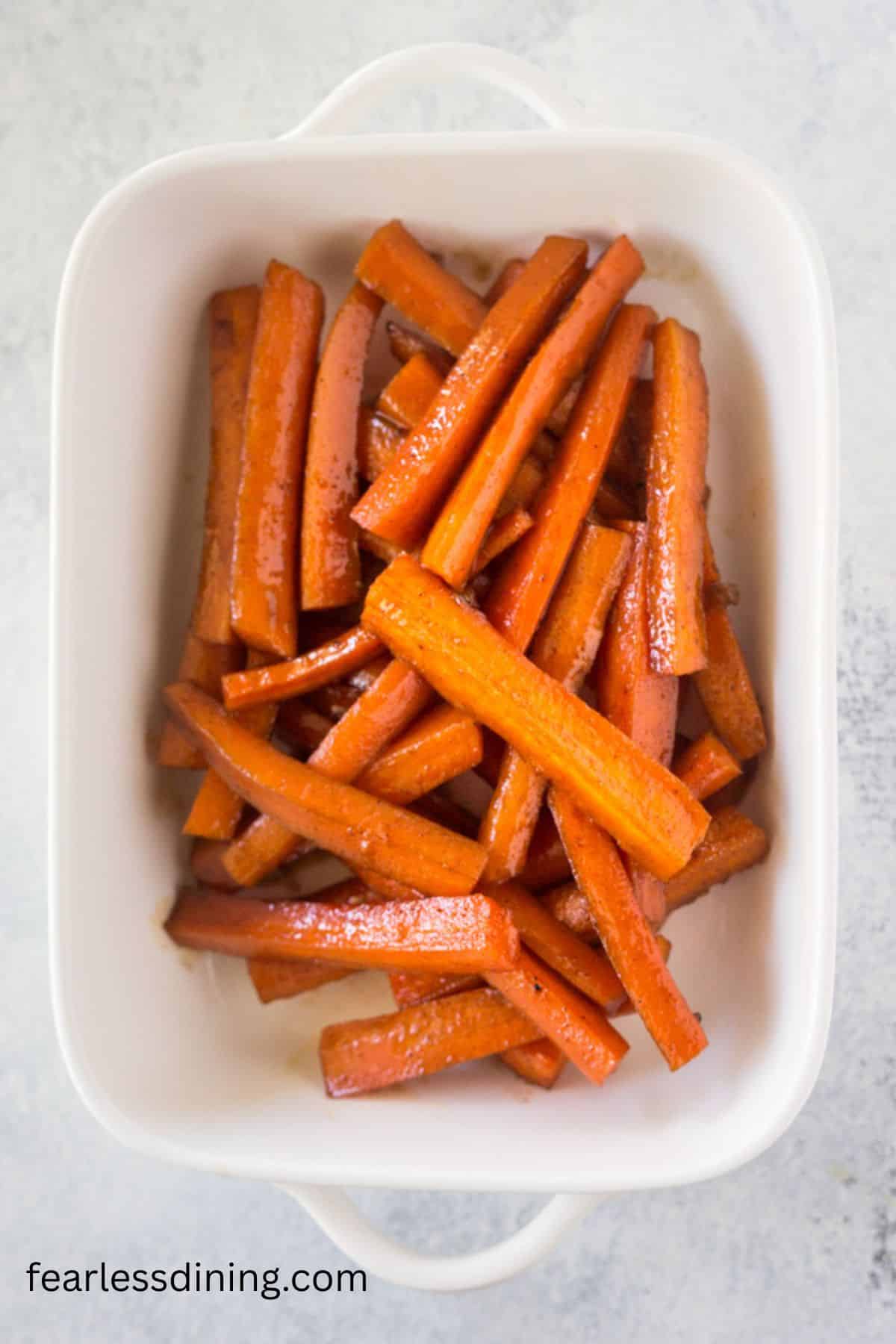 A white casserole dish with cooked cinnamon brown sugar carrots.