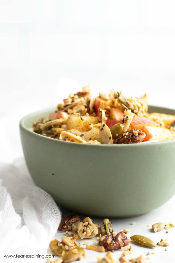 Granola topped cinnamon apples over yogurt in a green bowl.