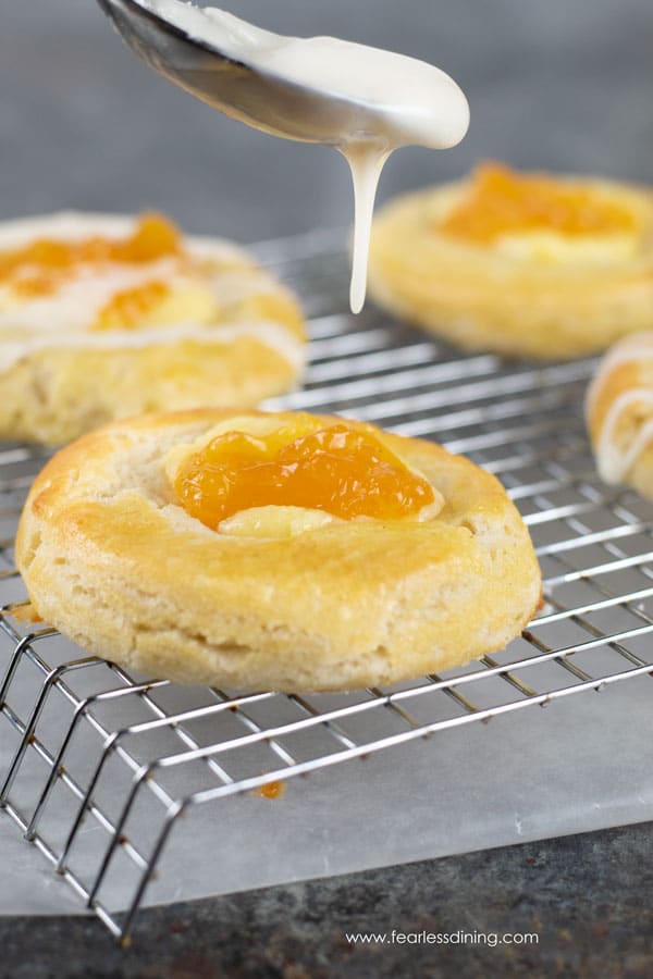 A spoon drizzling icing onto a gluten free cheese danish.