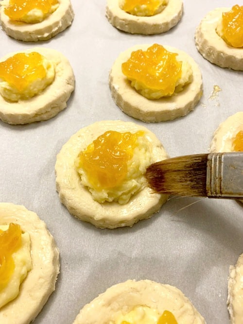 Using a brush to wipe egg wash onto each pastry.