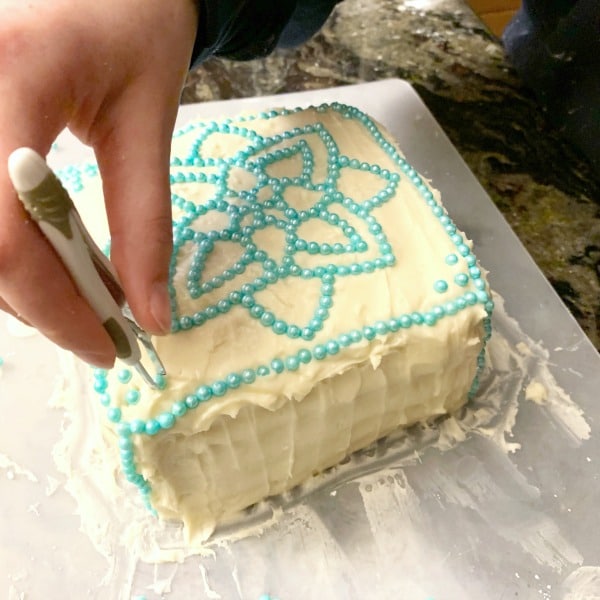 Using tweezers to drop sprinkles into a design on the cake.