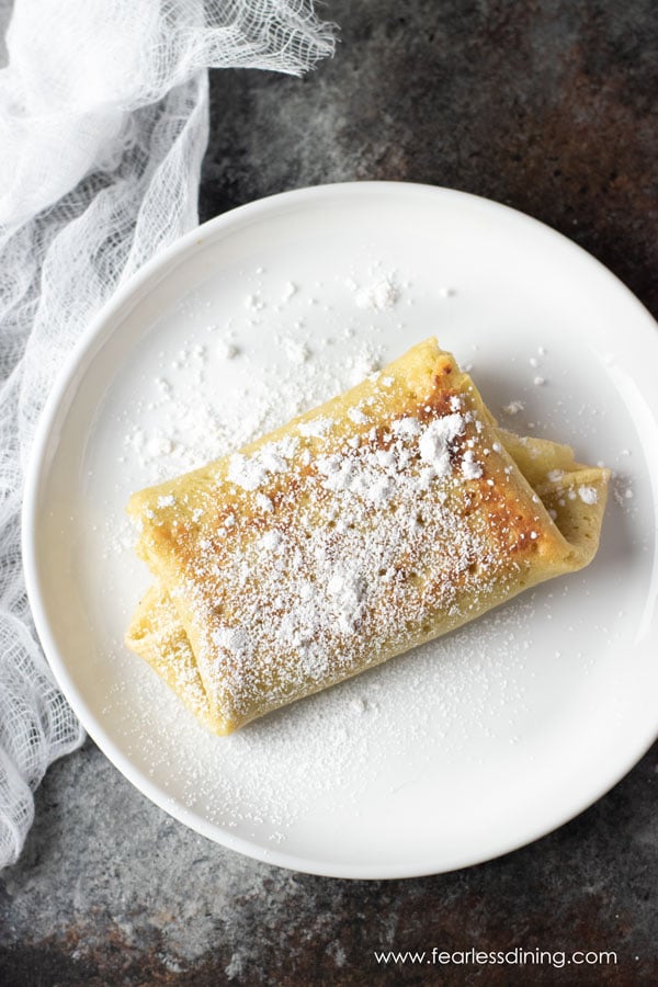 a folded cheese blintz on a plate with powdered sugar