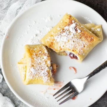 A cheese blintz cut in half on a plate so you can see the cheese and jam filling.