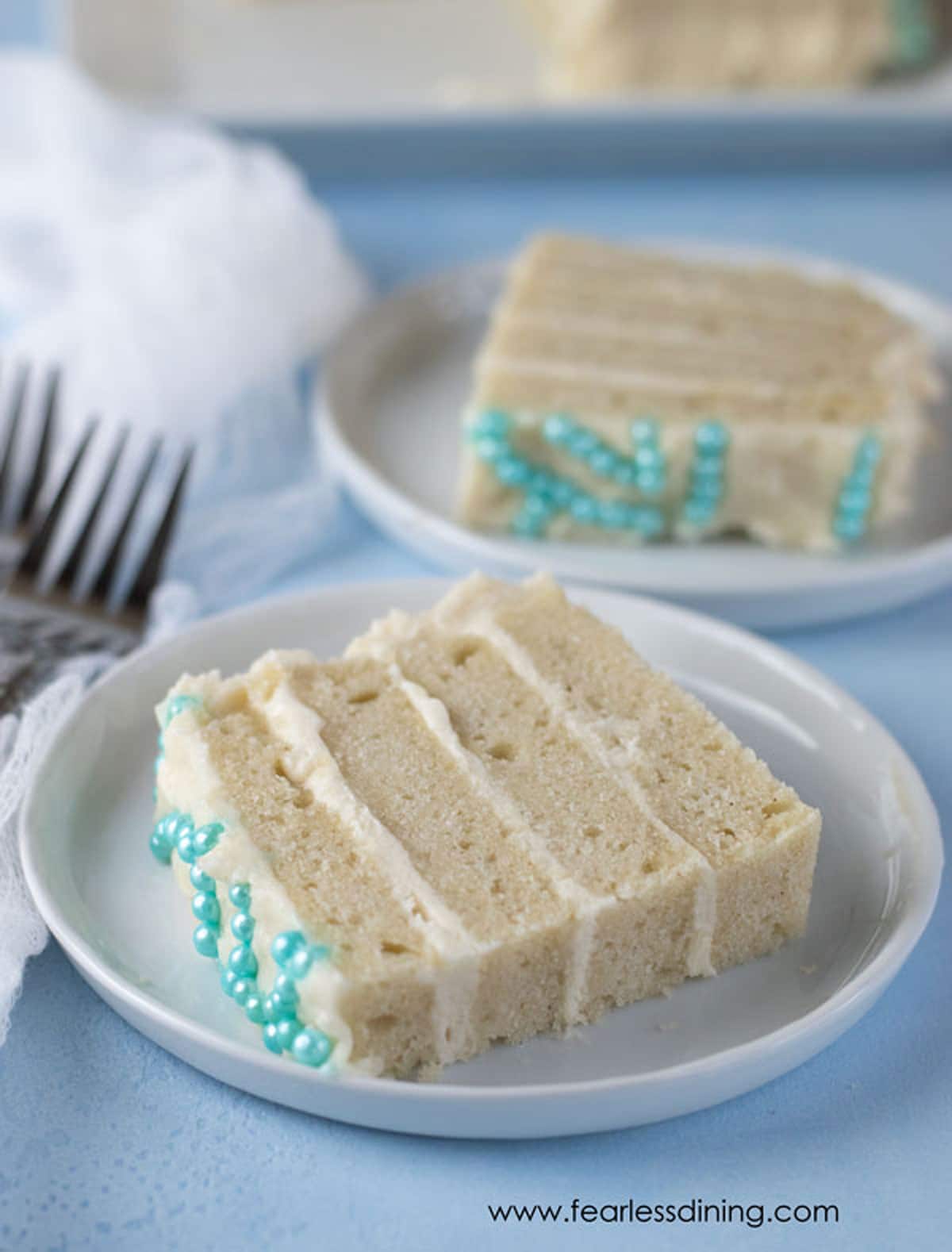 Two slices of vanilla cake on white plates.