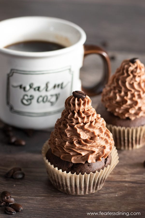 Two gluten free mocha cupcakes next to a mug of coffee.