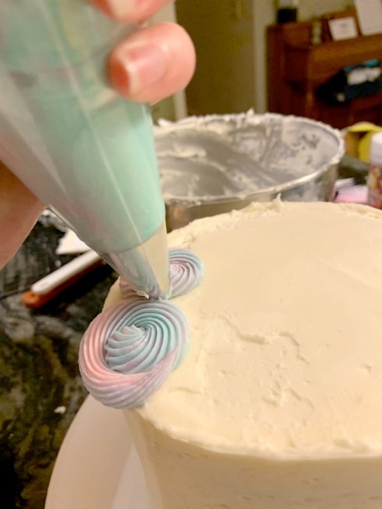 A frosting bag making rainbow frosting swirls on a cake.