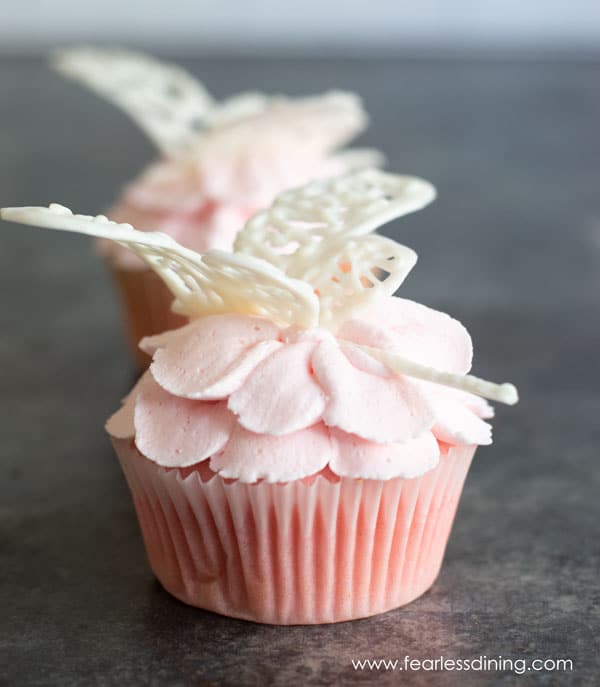 Dragonflies made out of white chocolate sitting on cupcake flowers.