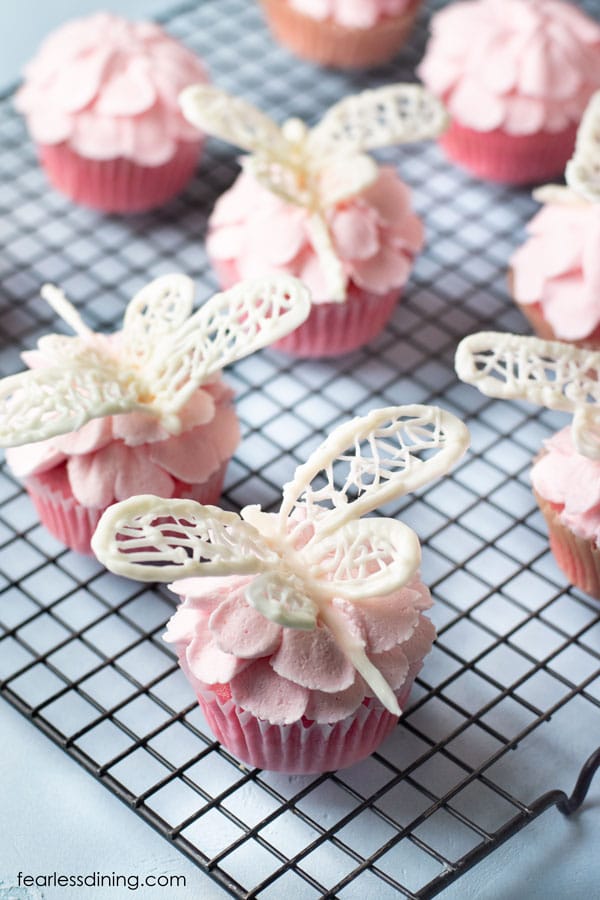 A rack of pink lemonade cupcakes with white chocolate dragonflies on top of them.