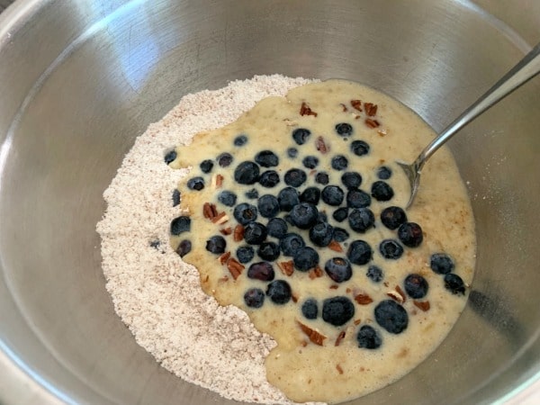 All of the muffin ingredients including blueberries in a bowl ready to mix.