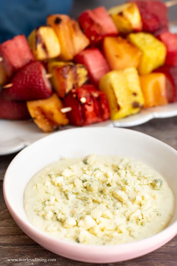 Grilled fruit kabobs next to a bowl of blue cheese dip.