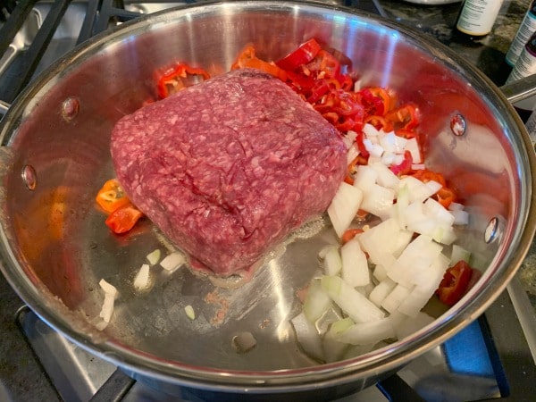 Ground hamburger meat, Italian Sweet Peppers, and onion in a frying pan.