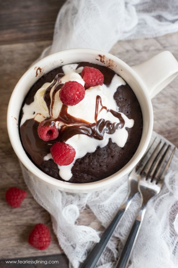 The top view of a chocolate mug cake topped with ice cream, hot fudge, and fresh raspberries.