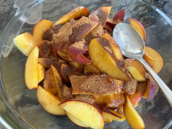 Sliced peaches in a a bowl with coconut sugar and honey.