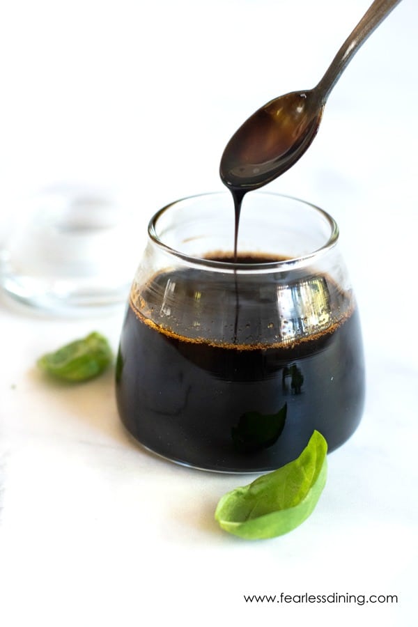 A spoon of the reductions sauce drizzling the sauce into a jar.