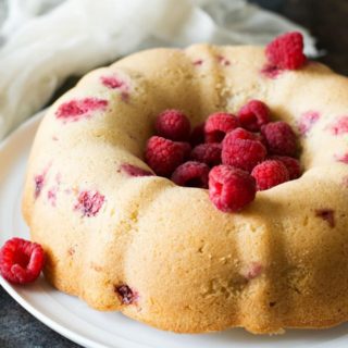 A vanilla bundt cake filled with fresh raspberries on a cake stand.