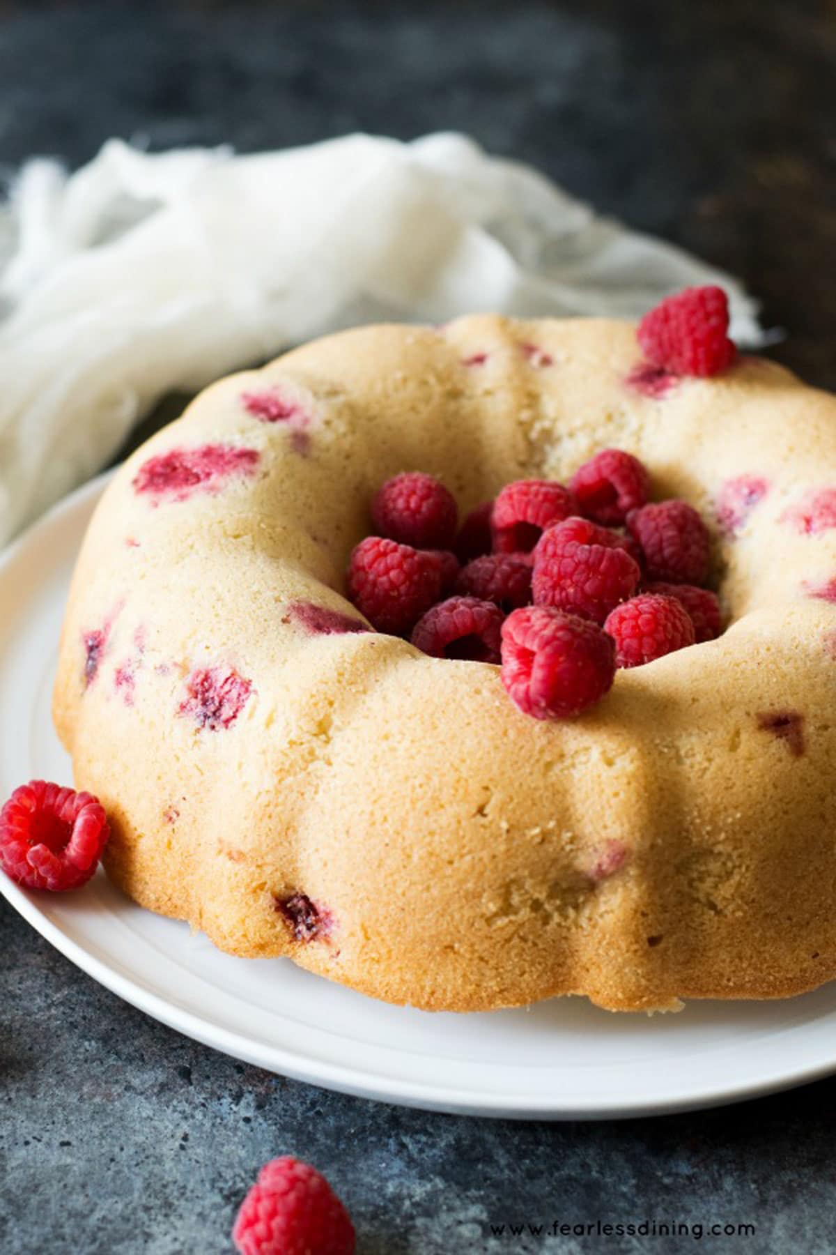 A vanilla bundt cake filled with fresh raspberries on a cake stand.