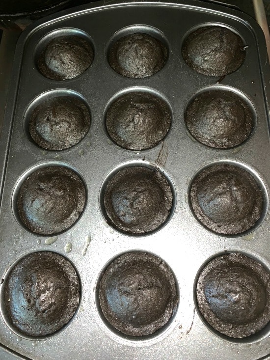 Baked black cupcakes in a muffin tin.