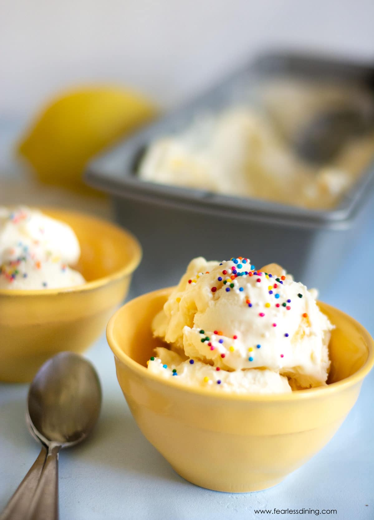 A yellow bowl filled with lemon ice cream. It is topped with rainbow sprinkles.