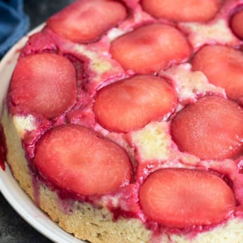A whole gluten-free plum upside down cake on a platter.