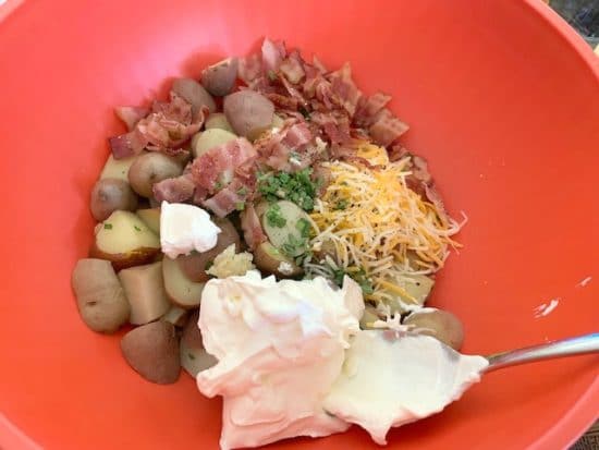 The bacon, potatoes, chives, cheese and sour cream in a bowl.